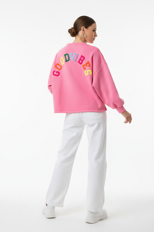 Model draagt het GOODVIBES Oversized Sweatshirt in roze met kleurrijk geborduurd logo op de rug