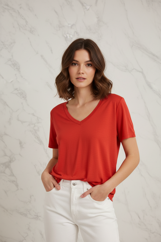 Model draagt de rode V-hals Top In April, gestijld met witte jeans in een casual chic editorial setting