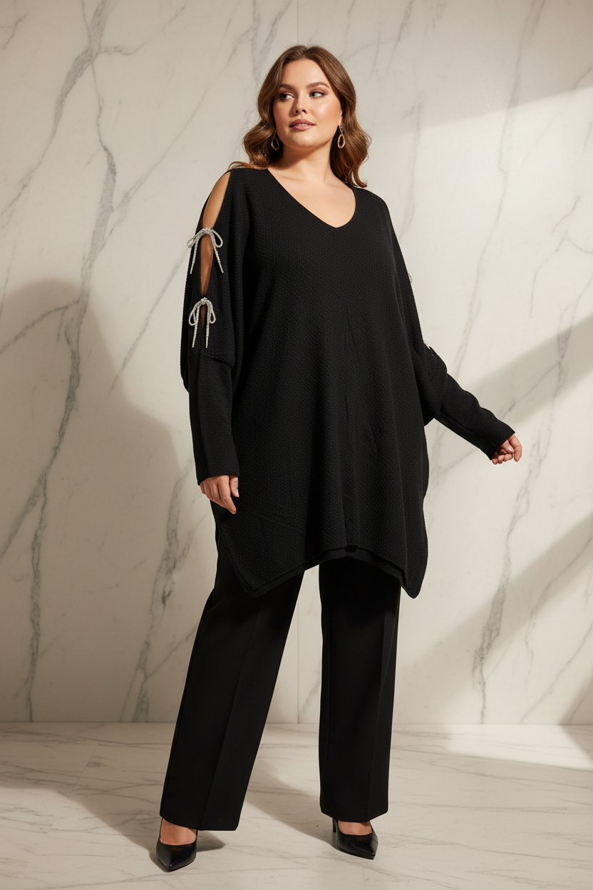 Model draagt de zwarte plus size Trui Times met open schouders en kristallen kettingen in een luxe editorial setting