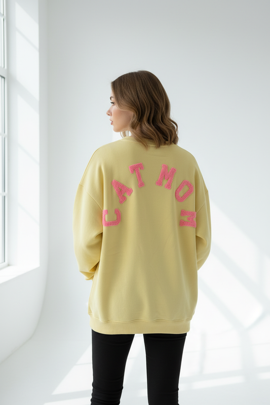 Model draagt gele CATMOM oversized sweatshirt met roze logo op de rug
