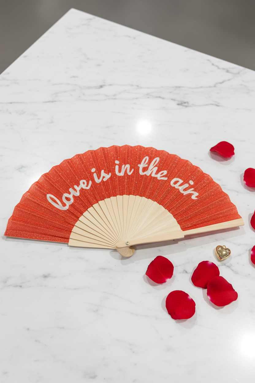Rode glitterwaaier Love is in the air met witte cursieve tekst en bamboe handvat