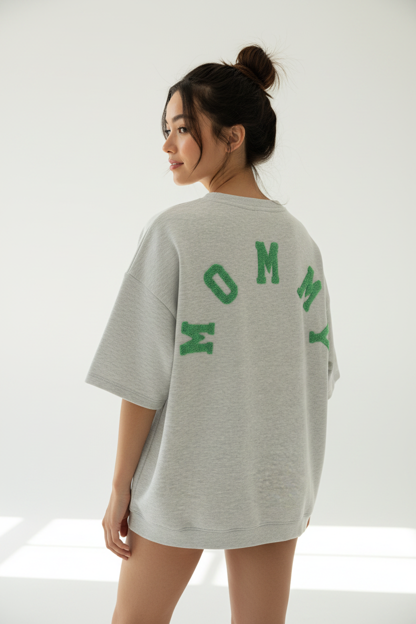 Model draagt grijze MOMMY oversized sweatshirt met groene chenille letters van achteren