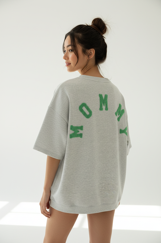 Model draagt grijze MOMMY oversized sweatshirt met groene chenille letters van achteren