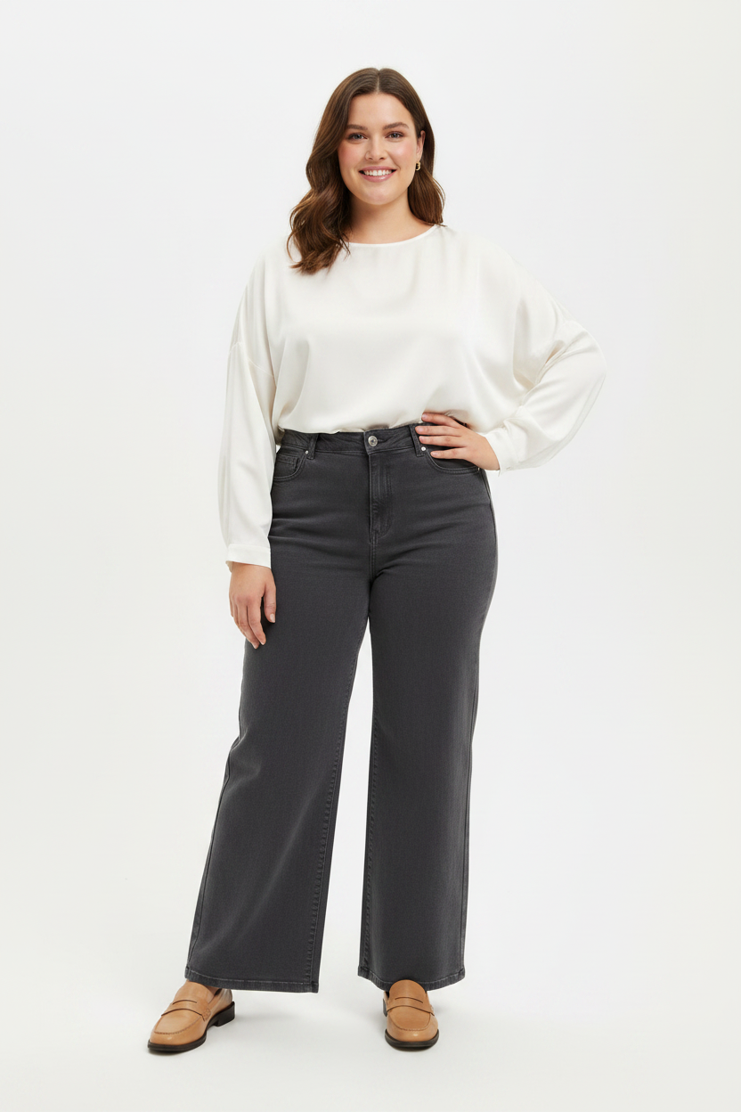 Plus-size model in grijze wide-leg jeans Goodies met crème blouse en loafers