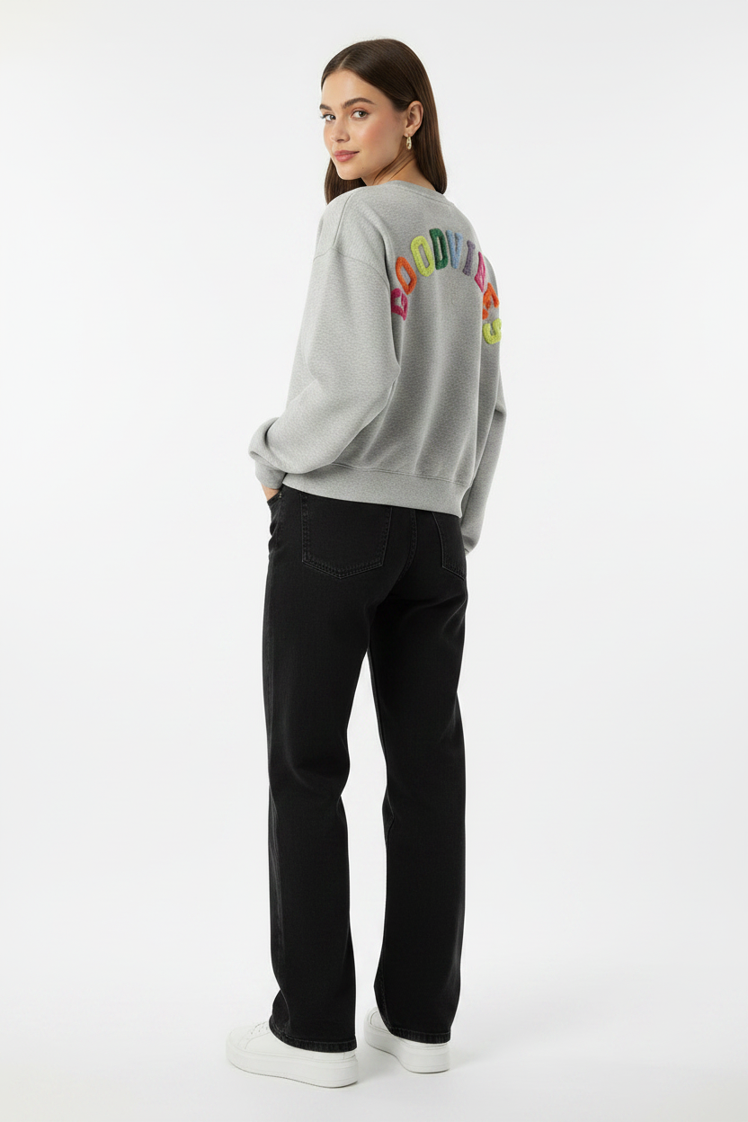 Model draagt het GOODVIBES Oversized Sweatshirt in grijs melange met kleurrijk geborduurd logo op de rug